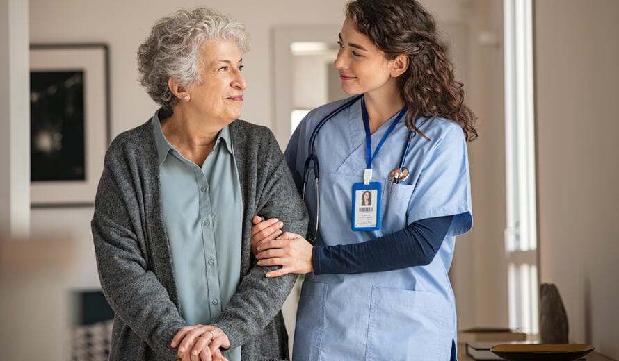 Young caregiver helping senior woman walking. Nurse assisting her old woman patient at nursing home. Senior woman with walking stick being helped by nurse at home.