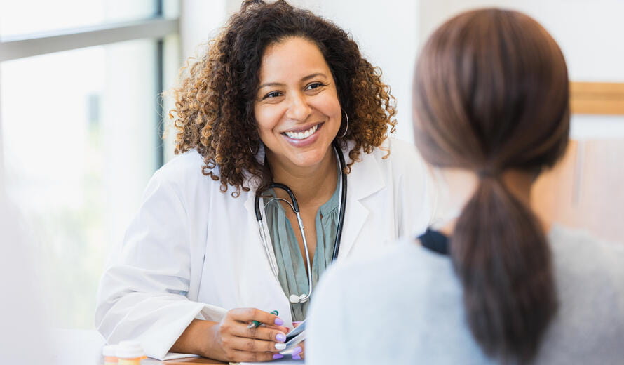 A smiling mid adult female doctor listens as a female patient discusses her health.