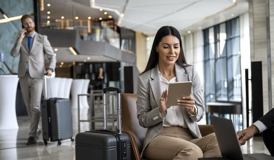 Focus on a young businesswoman holding her digital tablet and preparing for an important business meeting while her colleague is walking behind her and talking on the phone.