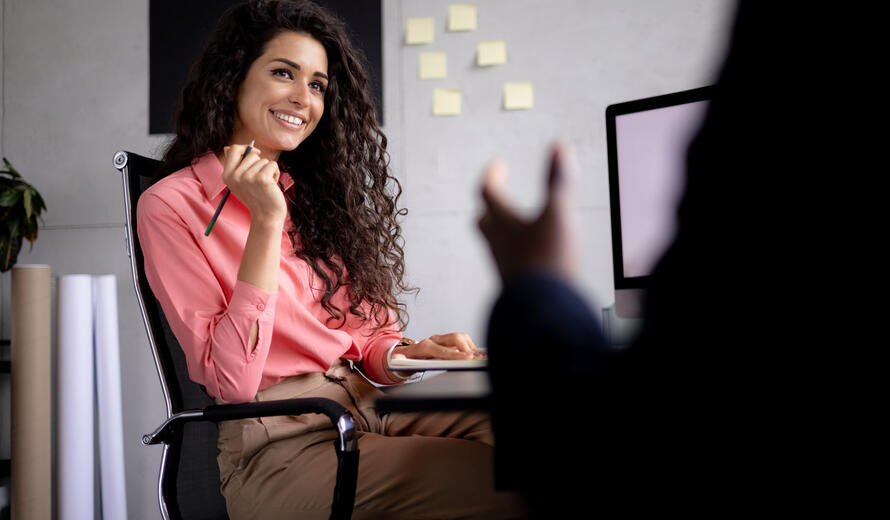 Happy female team leader having a meeting in her office meeting room with her male colleague and listening to him sharing his ideas with her