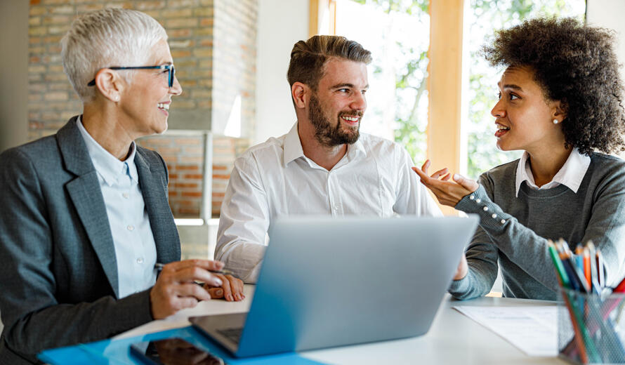 Image showing three individuals engaged in a discussion around a laptop.