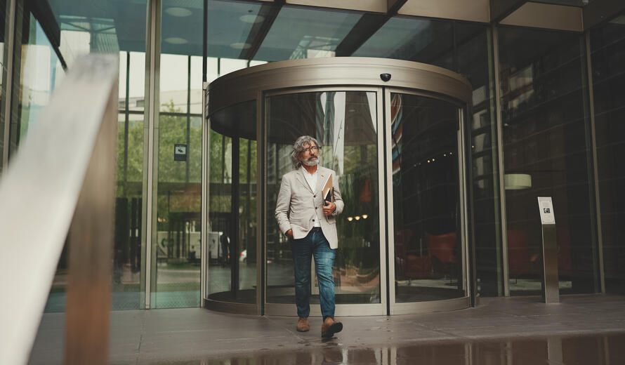  Mature businessman with beard in glasses wearing gray jacket holding folder with business documents is walking down the stairs leaving the business center