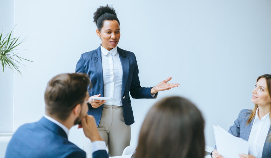 An employee in formal businesswear presents to colleagues, symbolizing effective corporate communication and professional occupation within a modern office environment