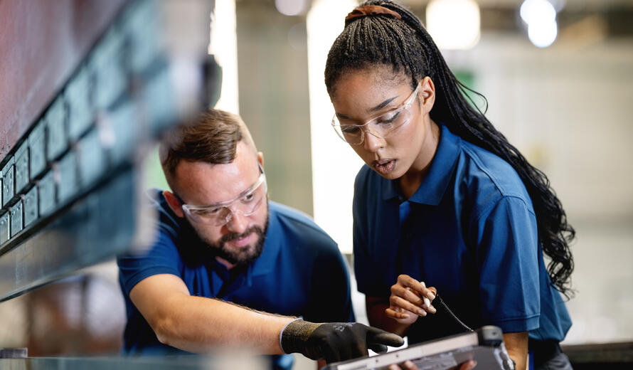 Manufacturing engineers analyzing equipment performance using tablet technology in factory.