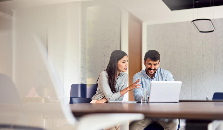 Two young professionals collaborating on a project, engaging with a laptop and exchanging ideas in a bright, modern office space filled with energy and creativity