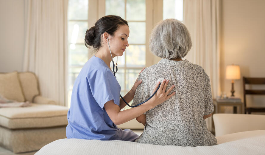 Nurse listening to chest of patient in home