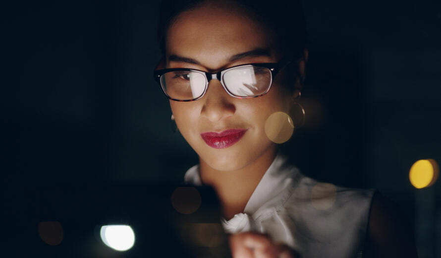 A young businesswoman uses a digital tablet while out in the city at night, showcasing modern technology in an urban setting.