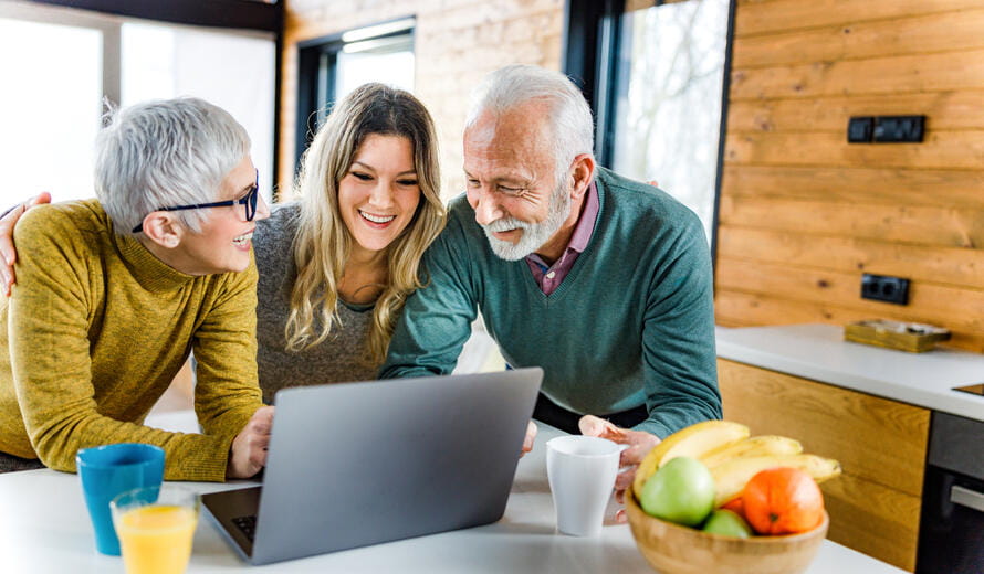 Happy senior parents and their adult daughter surfing the Internet on a computer at home.