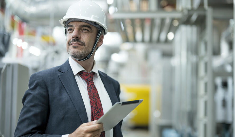 Confident businessman standing in the factory and holding digital tablet while working in boiler room control room of food processing plant.