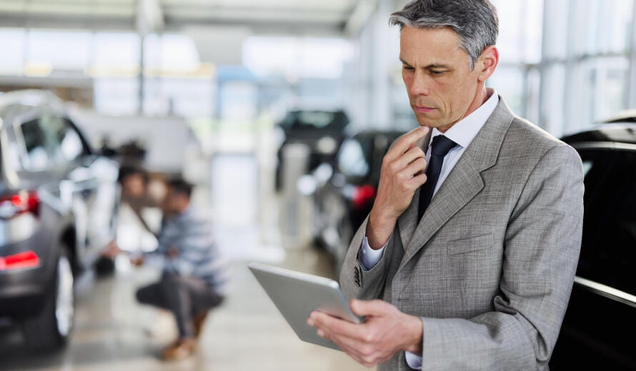 Mid adult manager reading an e-mail on touchpad in a car showroom.