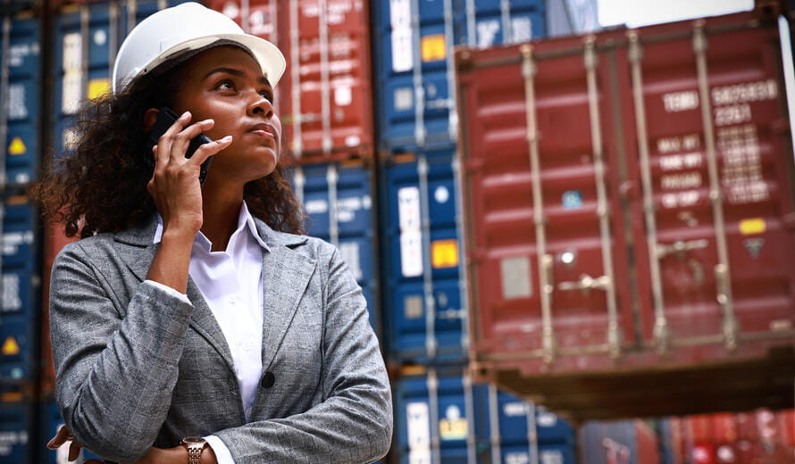 Portrait tanned woman in factory at container yard, Yong woman wearing safety helmet standing business discussion at container year, Logistic business and supply chain concept