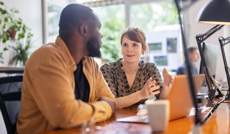 Woman with man sitting at desk and discussing new strategy. Business partners discussing a new project on a laptop computer in the office.