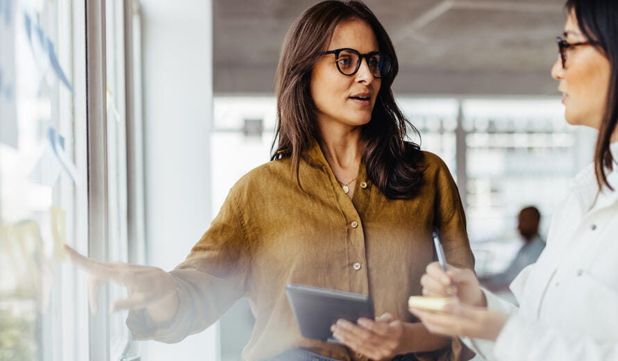 Business women discussing their ideas using sticky notes in an office. Female business professionals standing next to a window and brainstorming.