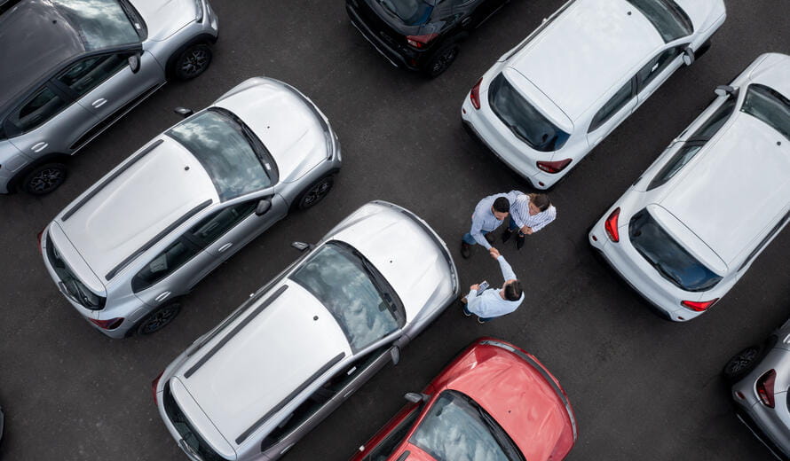 couple buying a car and closing a deal handshaking with the salesman