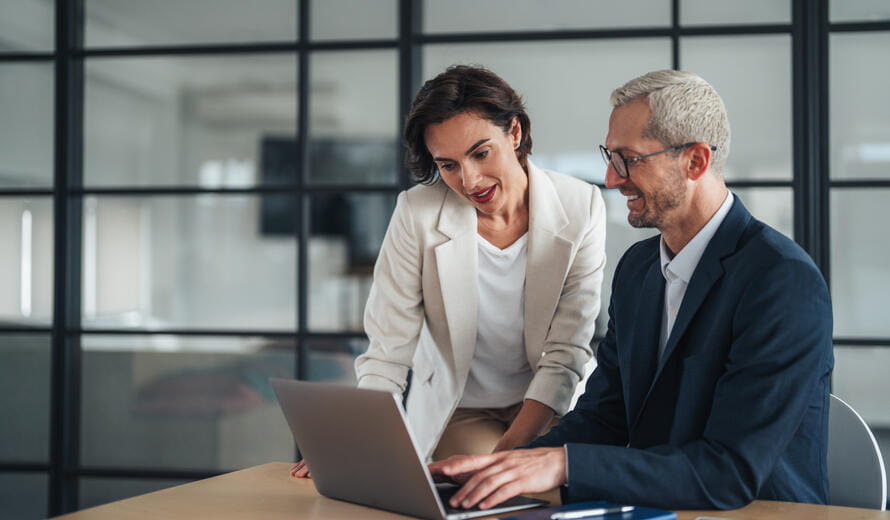 A focused businesswoman listens attentively during a strategic conversation with a male colleague in a contemporary office setting.