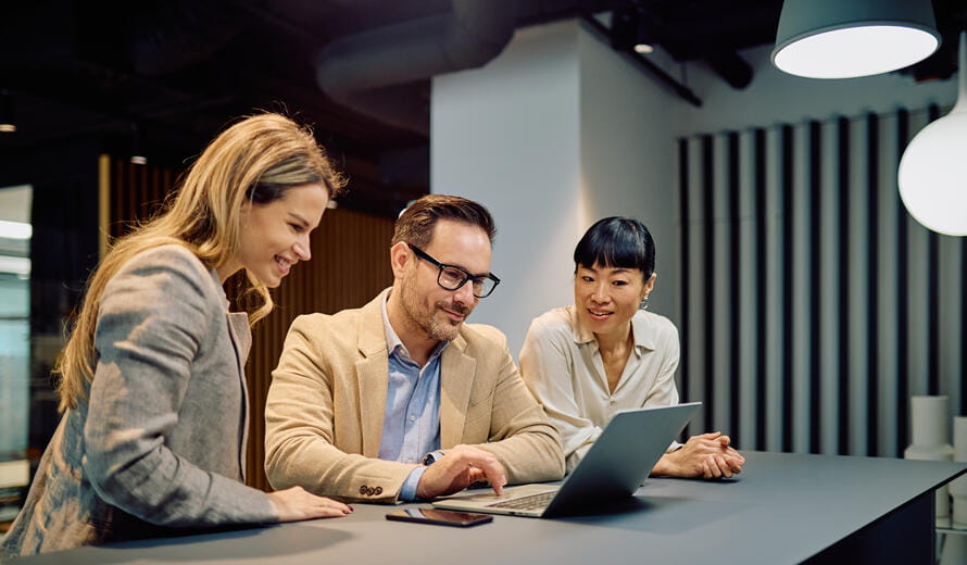 Diverse business professionals collaborating, working together on a laptop, sharing ideas and discussing strategy in a modern office