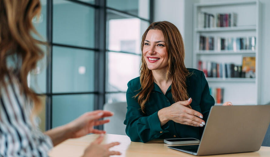 a professional discussion between two individuals in an office setting using a laptop